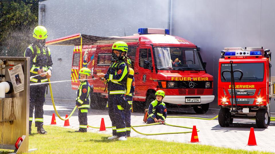 Feuerwehrkinder in Schutzausrüstung ziehlen mit Wasserstrahl auf Übungsplatte
