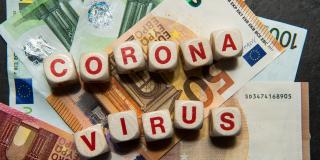 Würfel bilden die Wörter Corona und Virus. Sie liegen auf Banknoten.