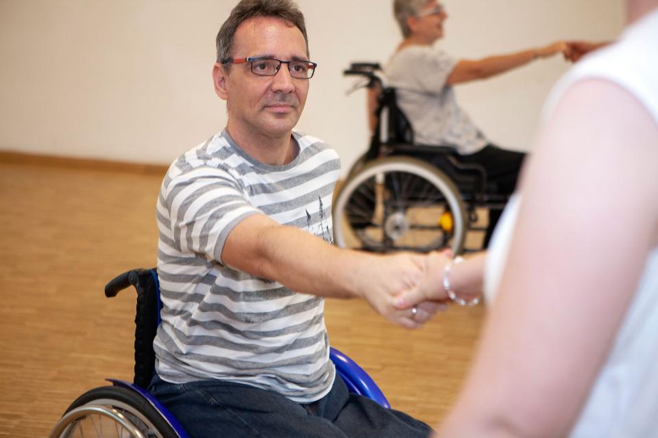 eine Person im Rollstuhl gibt einer anderen, die nicht im Rollstuhl ist die Hand beim tanzen