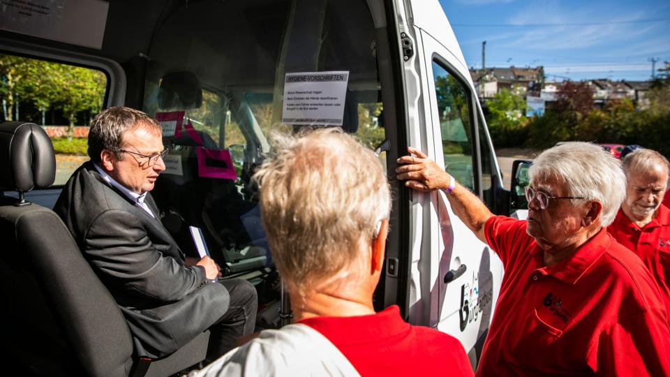 Oliver Krischer sitzt in einem Kleinbus und unterhält sich mit Busfahrer/innen