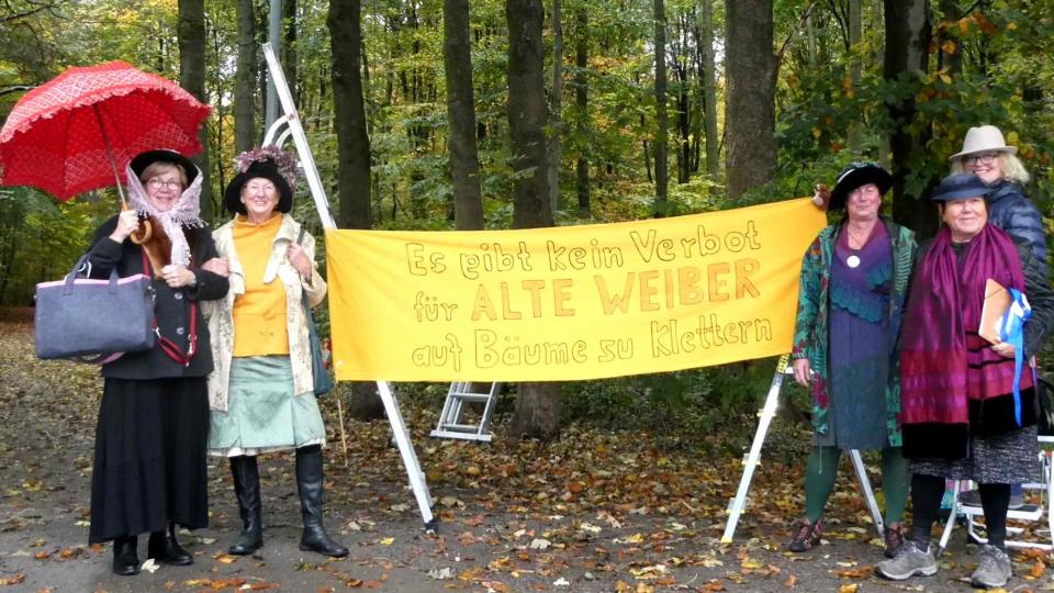 Fünf Frauen stehen mit einem Transparent mit der Auschrift "Es gibt kein Verbot für alte Weiber auf Bäume zu klettern" im Wald.