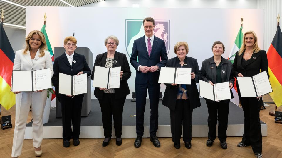 Ministerpräsident Hendrik Wüst und die sechs Landesverdientsordenträgerinnen mit Urkunde