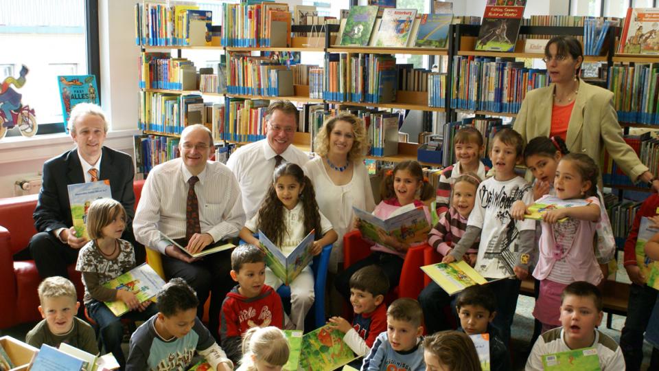 Gruppe von Kindern und Erwachsenen, die Bücher in ihren Händen halten.