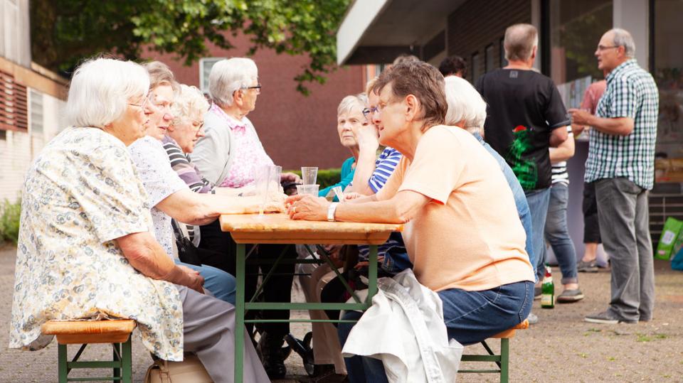 Senioren sitzen sich auf Bierbänken gegenüber und unterhalten sich. 