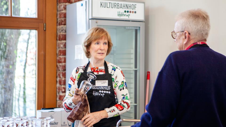 Kulturbahnhof Hiltrup: Helferin putzt Gläser hinter der Theke und unterhält sich. 