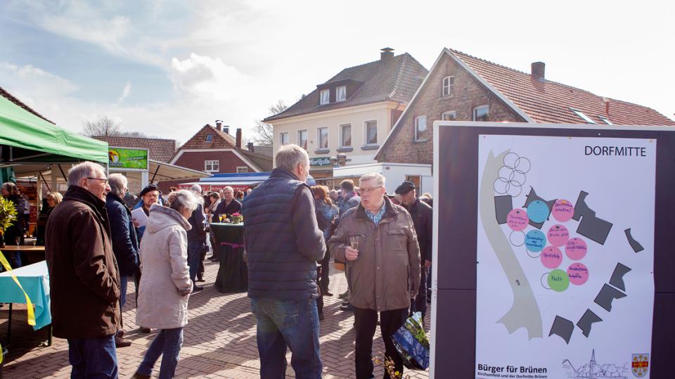 Bürger für Brünen e.V.: Bürger/innen diskutieren auf Dorfplatz vor Karte zur Dorfmitte
