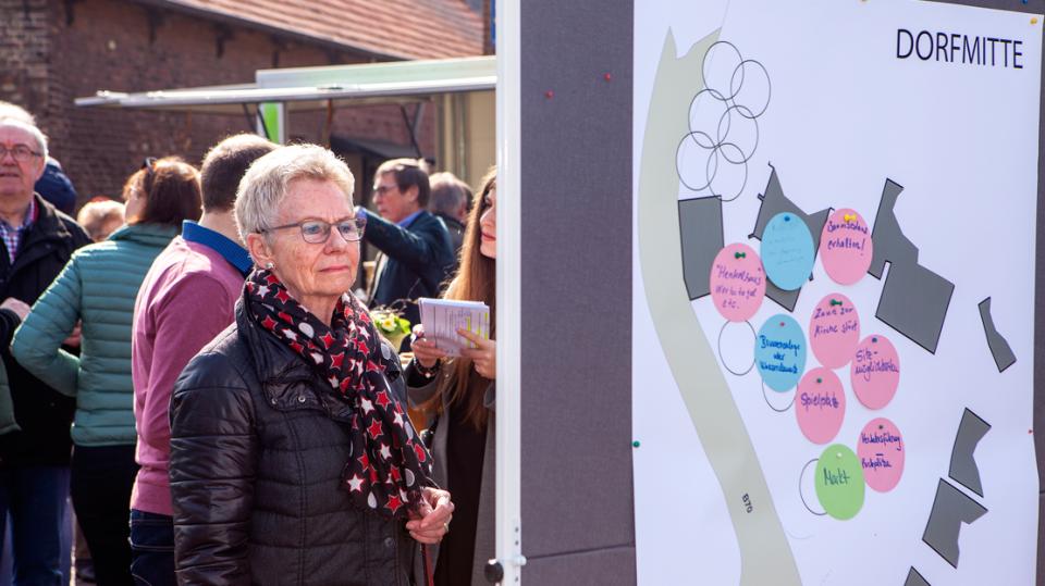 Bürger für Brünen e.V.: Dame betrachtet Pinnwand mit Plänen zur Dorfmitte