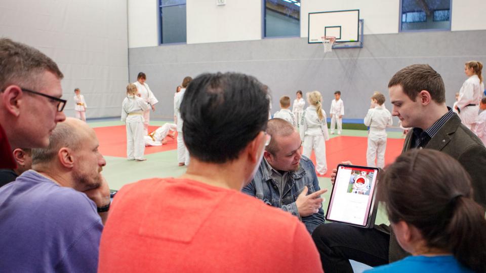 Judo Hilden: Besprechung mit Tablet, Judo-Training im Hintergrund