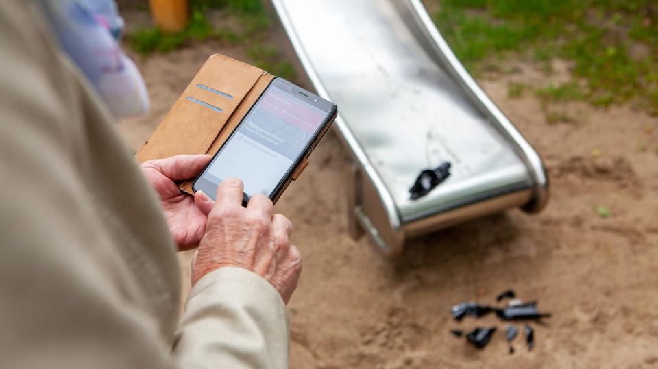Ältere Dame nutzt Smartphone wegen kaputten Flaschen auf Spielplatz