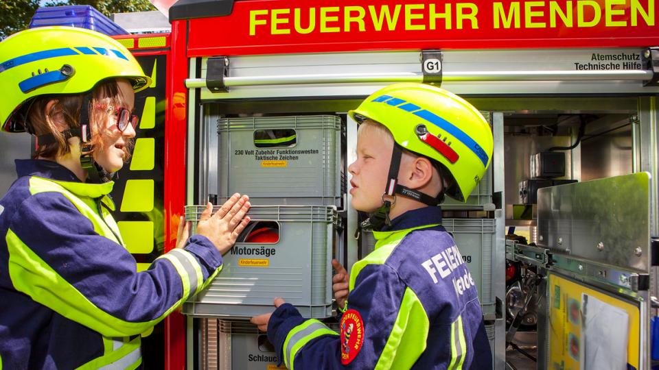 Zwei Kinder in Uniformen der Feuerwehr Menden mit Materialkiste an der Miniaturausgabe eines Löschfahrzeugs
