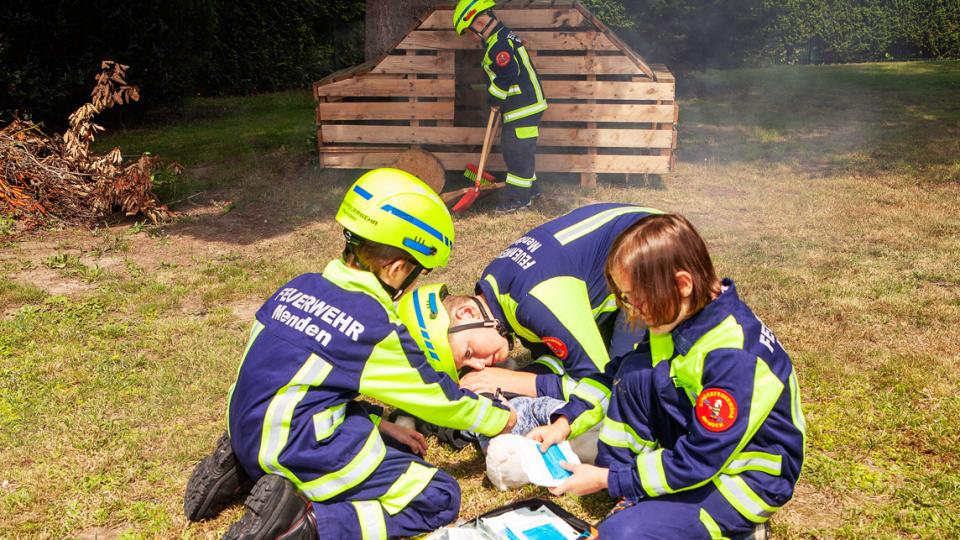 Kinder in Feuerwehruniform führen Übungen in Erster Hilfe und Wiederbelebungsmaßnahmen am Stofftier durch