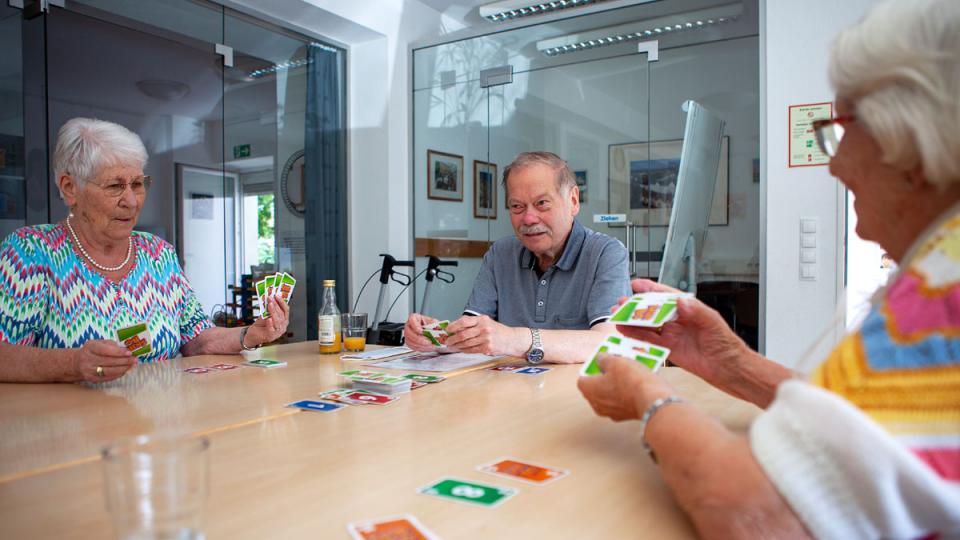 Drei Menschen spielen im Besprechungsraum am Tisch Karten