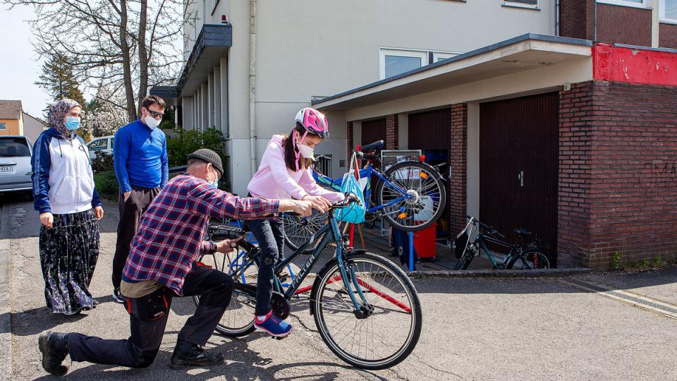 Mädchen mit Fahrradhelm auf einem Fahrrad, das noch von einem Mann am Hinterrad überprüft wird