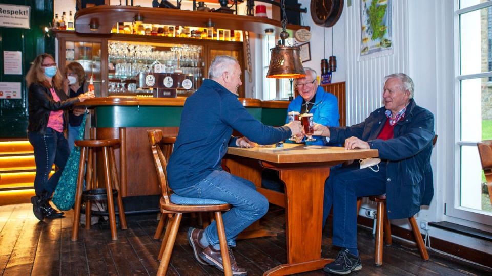 Drei Männer sitzen in der Kneipe am Tisch und heben ihre Biergläser zum Anstoßen