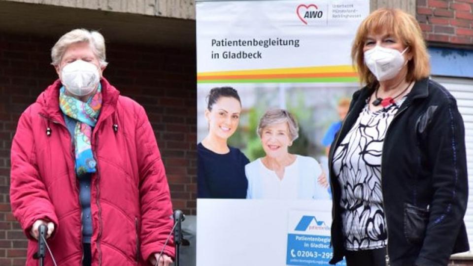 Zwei Frauen stehen links und rechts vor Werbebanner der »Patientenbegleitung in Gladbeck«