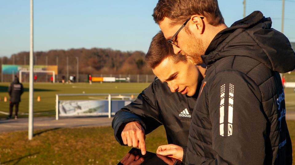 Trainer und Junge schauen gemeinsam neben dem Fussballtrainingsplatz auf ein Tablet