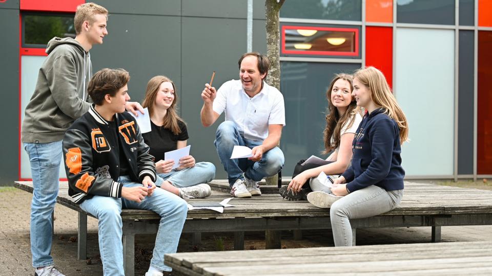 fünf Schüler/innen und ein Lehrer sitzen auf einer Plattform im Schulhof und diskutieren