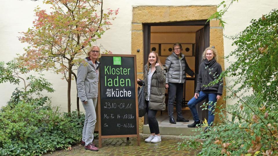 vier Personen stehen vor einer Tür, neben ihnen ist eine Klapptafel mit der Aufschrift »Klosterladen alte Küche« zu sehen