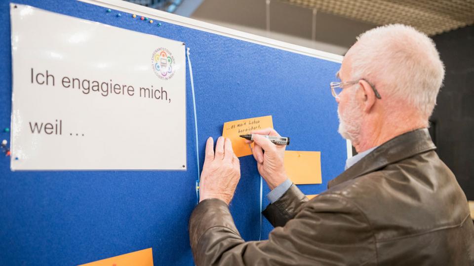 Engagementkongress Siegen: Mann hängt Zettel zu "Ich engagiere mich, weil..." an Pinwand.