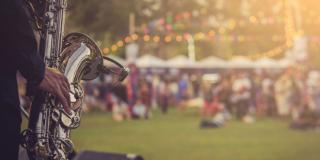 Musiker spielt Saxophon auf einer Außenbühne, Menschen auf Festwiese unscharf erkennbar