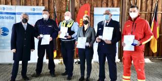 Minister Reul auf einem Gruppenbild mit Helferinnen und Helfern der Unwetterkatastrophe 2021, die Medaillen und eine Urkunde in der Hand halten.