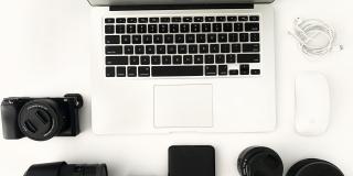 Laptop, Maus, Kopfhörer, Festplatte, Musikbox, Kamera und diverse Objektive auf einem weißen Hintergrund